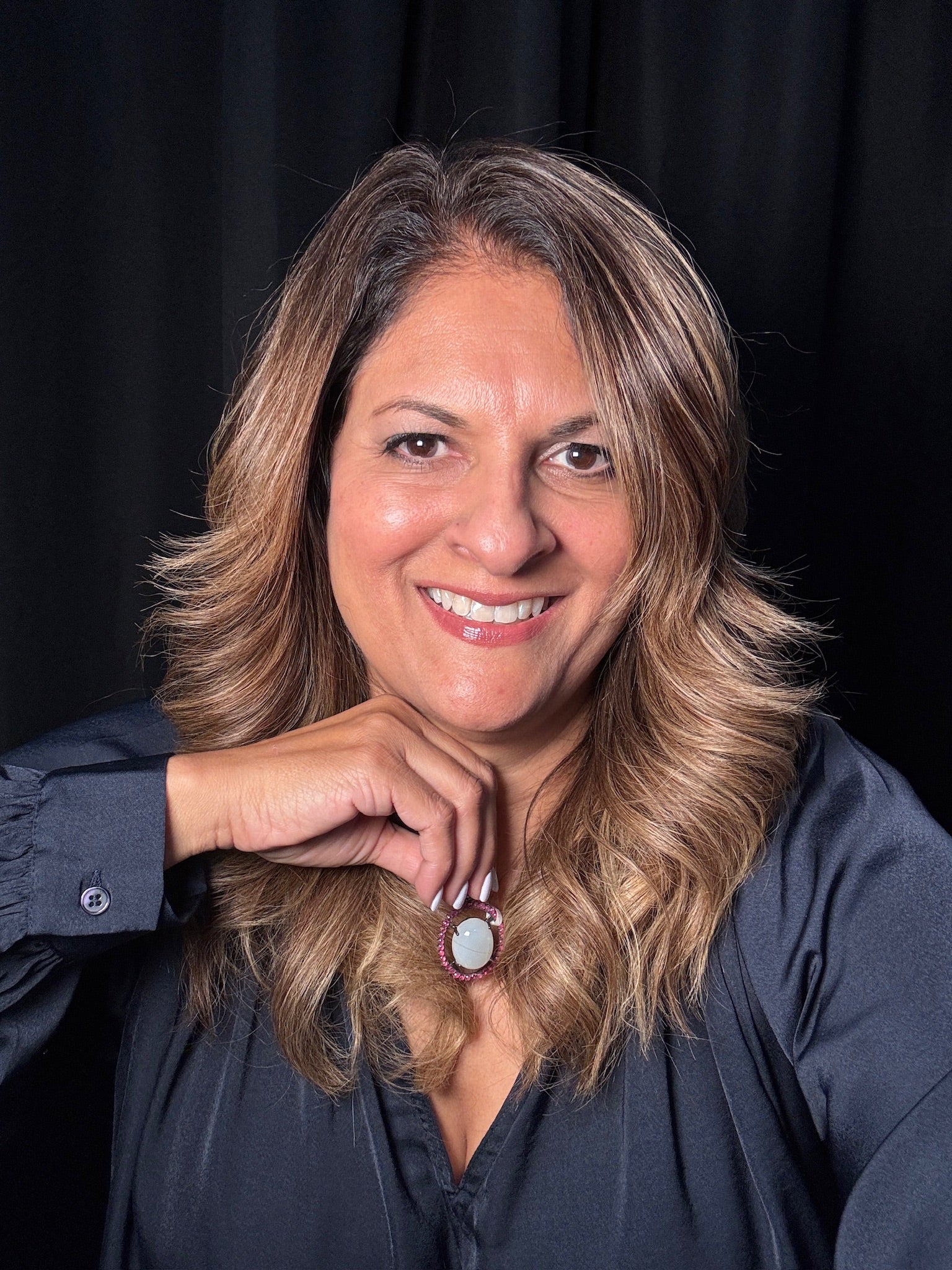 Smiling woman wearing a moonstone and ruby pendant with white center stone and pink ruby halo in sterling silver setting against dark background