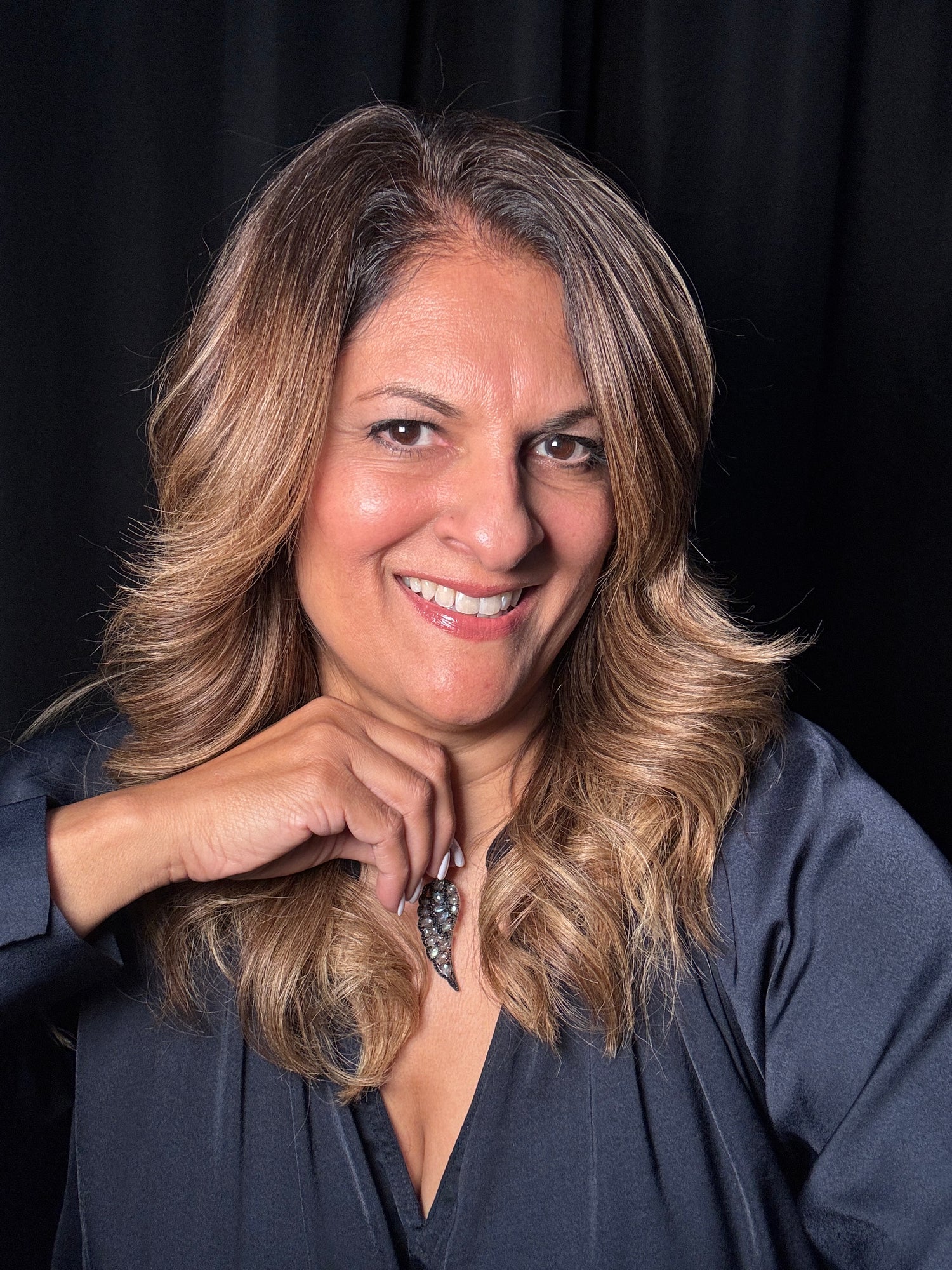 Woman with blonde wavy hair smiling while wearing the labradorite and black spinel wing pendant on sterling silver chain