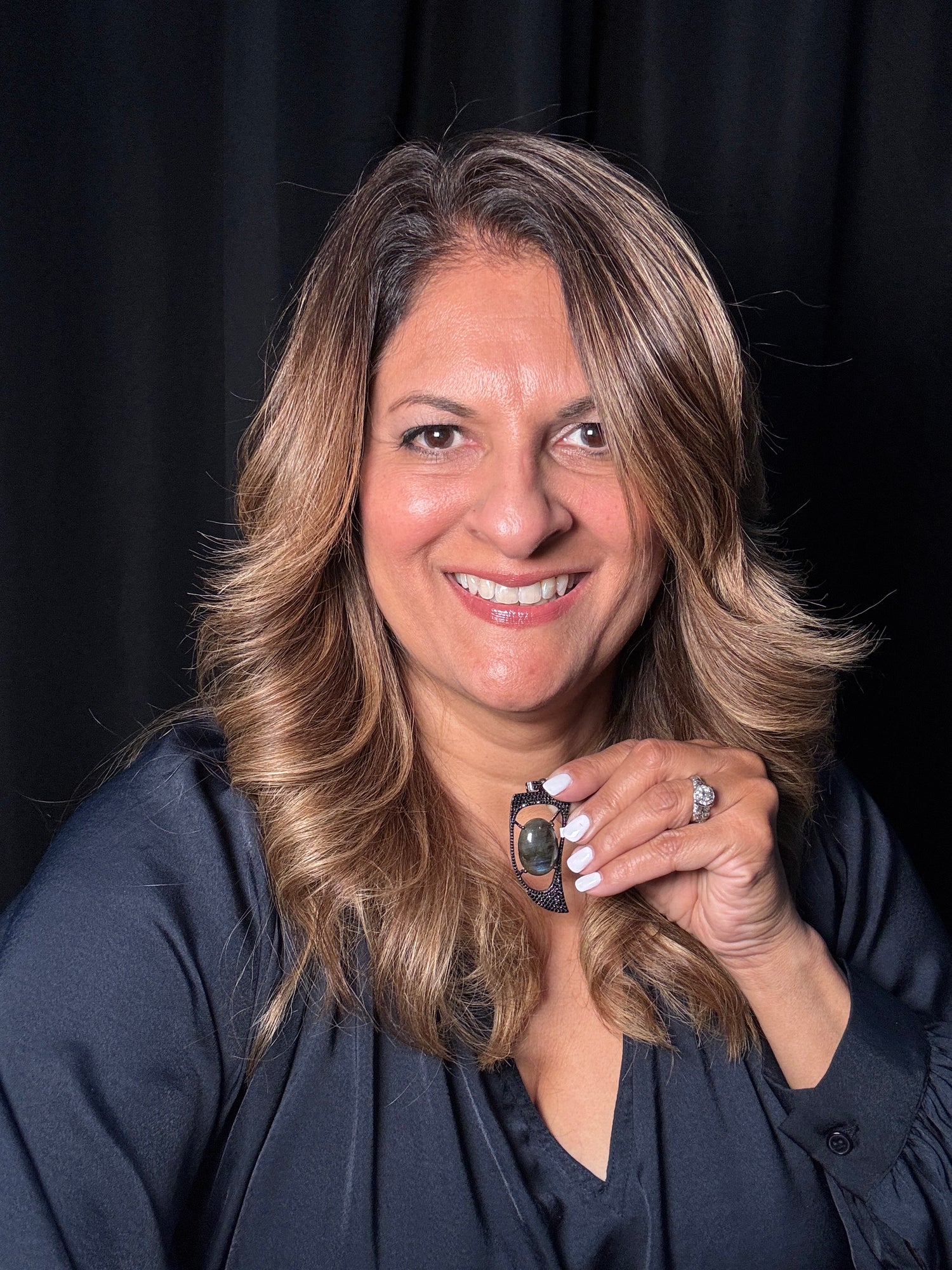 Smiling woman wearing statement labradorite and black spinel horn pendant, showcasing the dramatic curved design and iridescent gemstone center