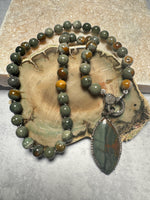 Full flat lay of Rocky Butte jasper necklace on petrified wood slice, displaying complete 18-inch length with diamond clasp and marquise pendant