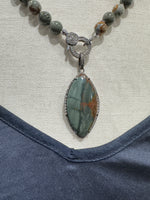 Close-up flat lay of Rocky Butte jasper necklace on neutral fabric, highlighting diamond toggle clasp and sculpted sterling silver marquise pendant detail