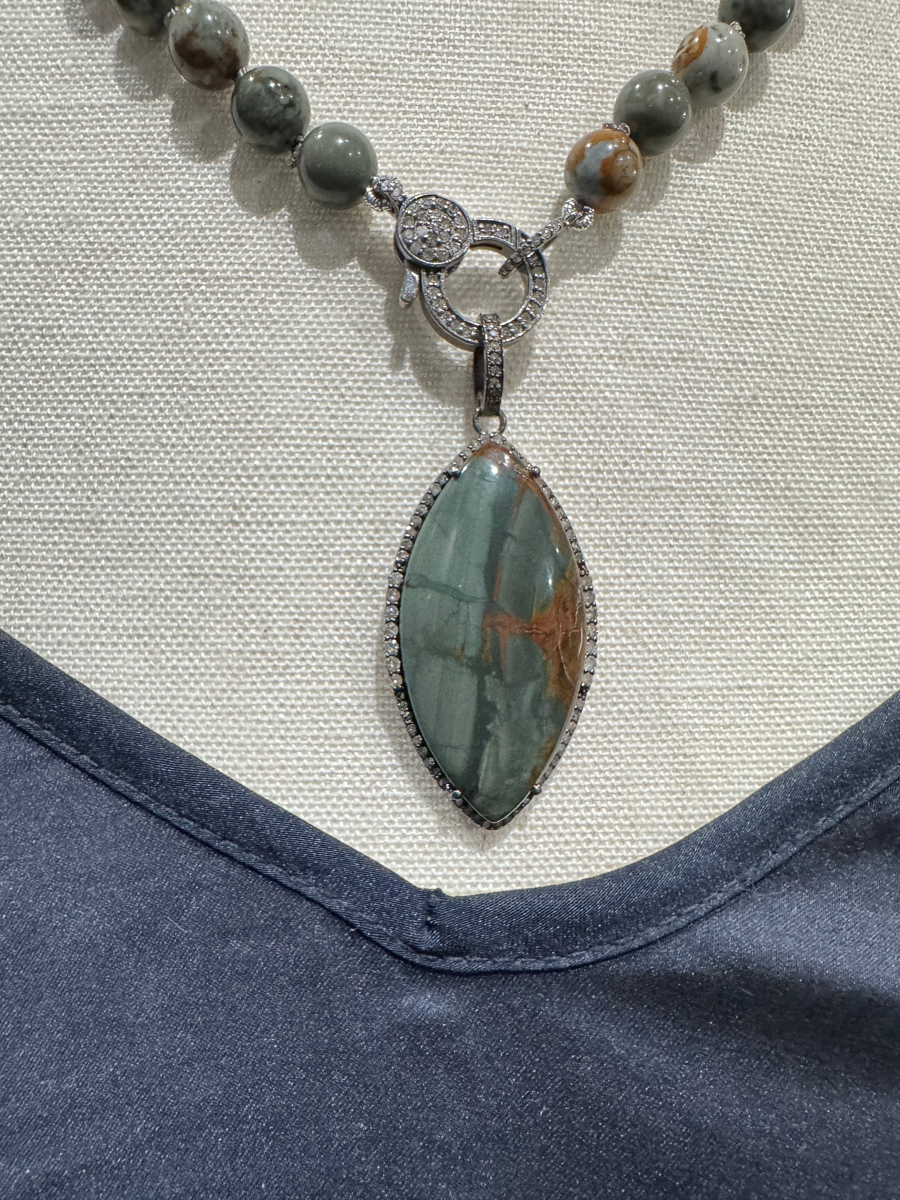 Close-up flat lay of Rocky Butte jasper necklace on neutral fabric, highlighting diamond toggle clasp and sculpted sterling silver marquise pendant detail