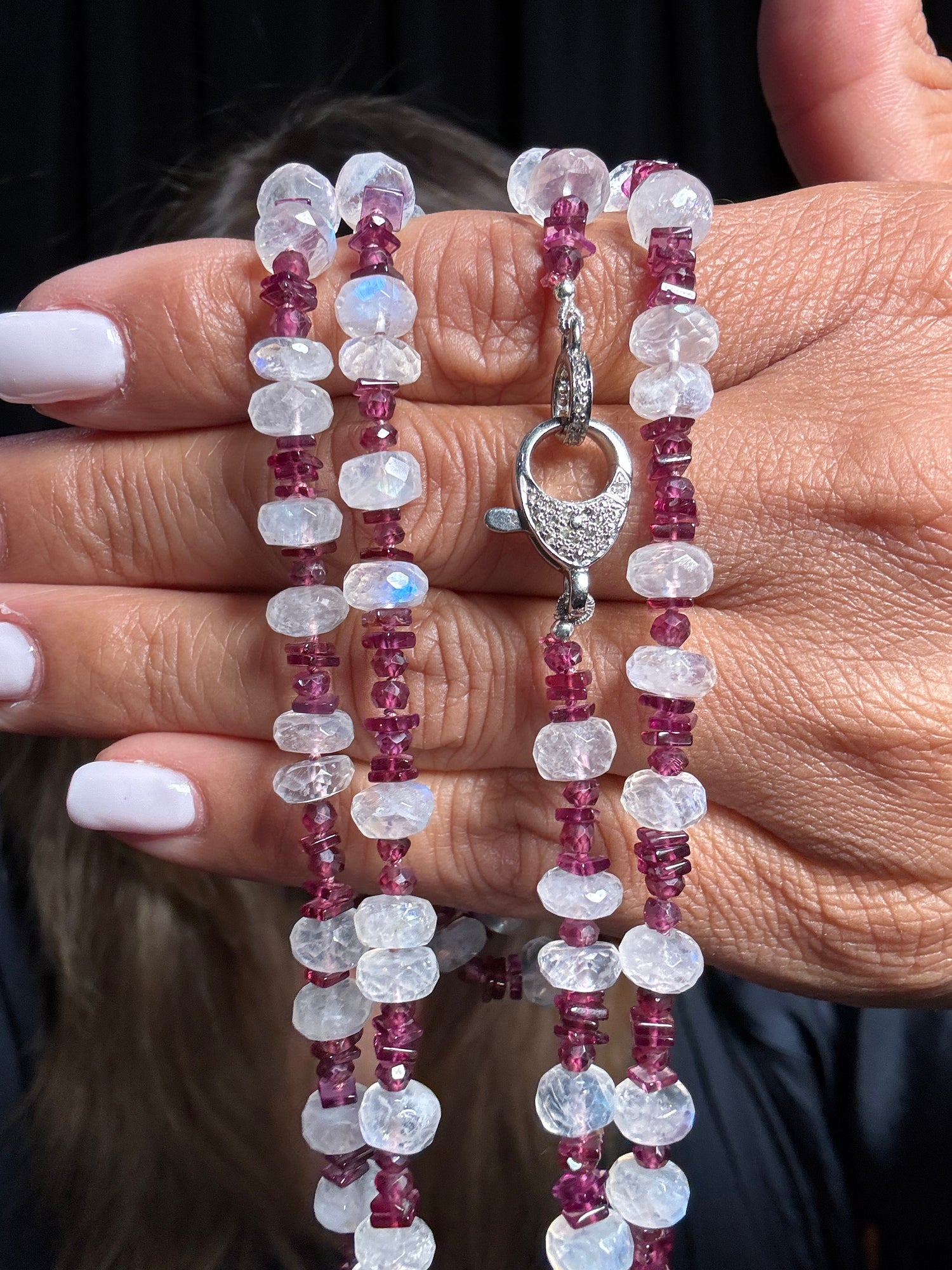 Close-up of hands holding a 34-inch necklace featuring alternating clear moonstone and deep red rhodolite garnet beads with a sterling silver diamond-accented clasp