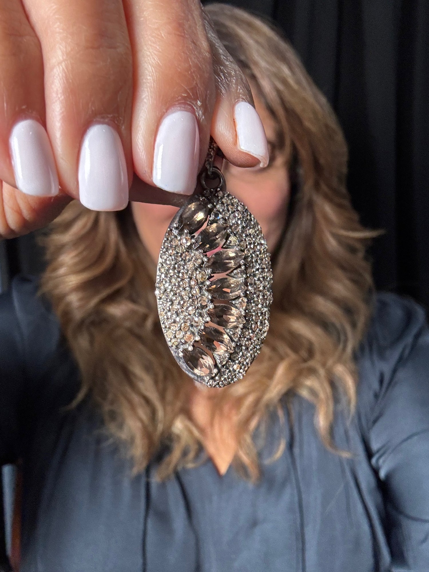 Hand holding an oval smoky topaz and diamond pendant on sterling silver chain, featuring brown gemstone center surrounded by sparkling diamonds