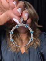 Blue topaz crescent pendant with diamonds held in hand, showing six teardrop blue topaz stones and sparkling diamond pave setting in sterling silver