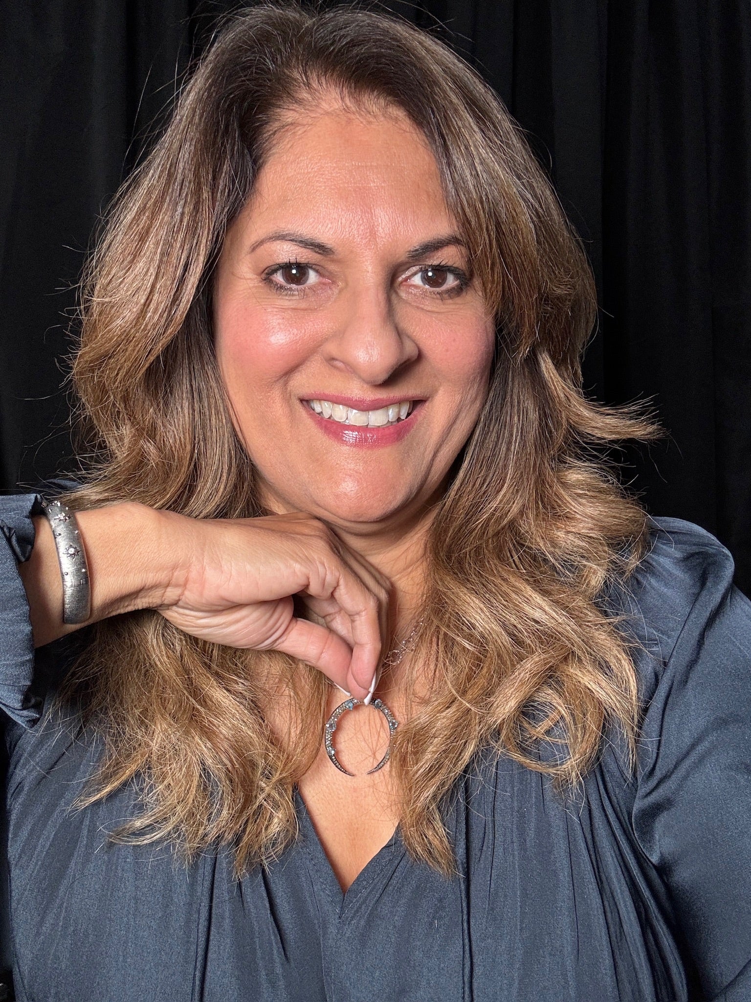 Woman wearing blue topaz crescent pendant necklace, displaying the curved crescent shape with blue gemstones against a gray top
