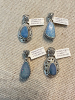 Four sterling silver Australian opal pendants displayed on natural burlap fabric, featuring blue opals in ornate and simple settings with price tags