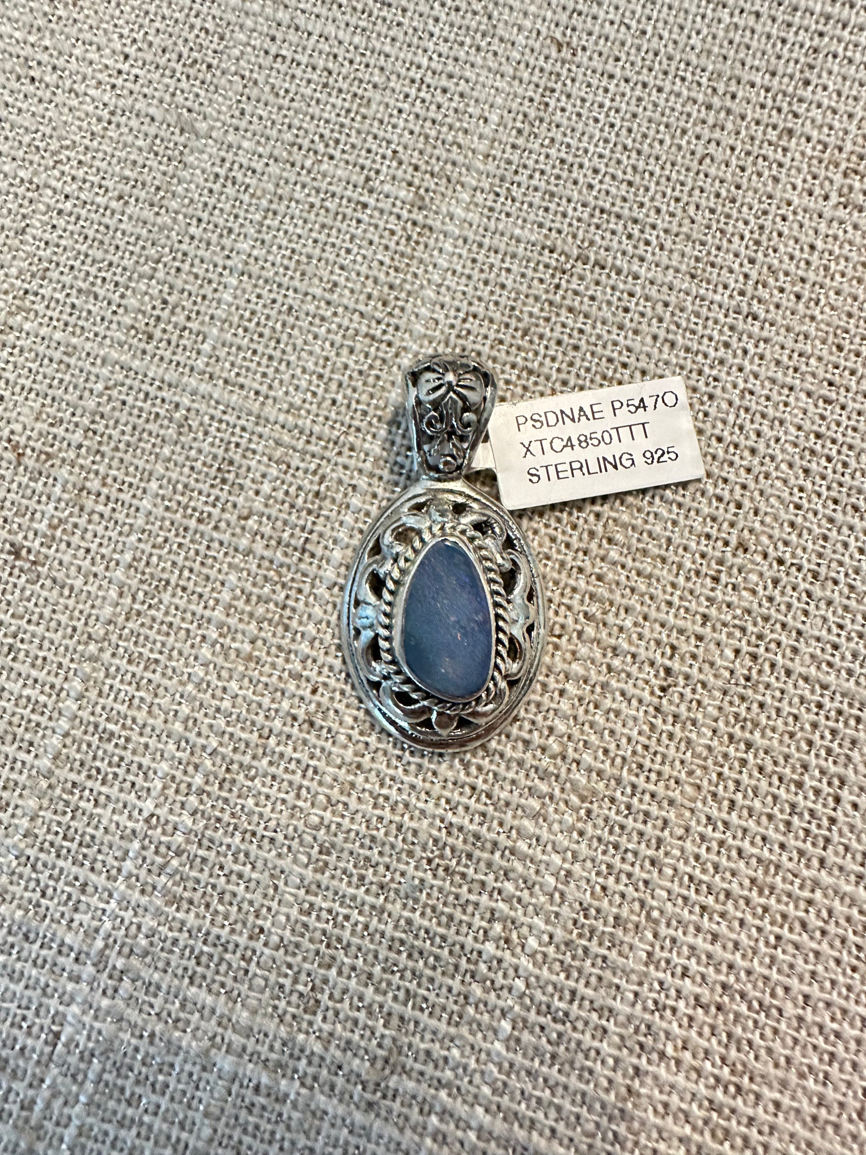 Oval blue Australian opal in ornate sterling silver filigree setting with decorative scrollwork border, photographed flat on burlap fabric
