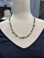 Close-up view of Ethiopian opal and London blue topaz necklace on cream mannequin, highlighting the contrast between luminous white opal discs and rich blue topaz gemstones