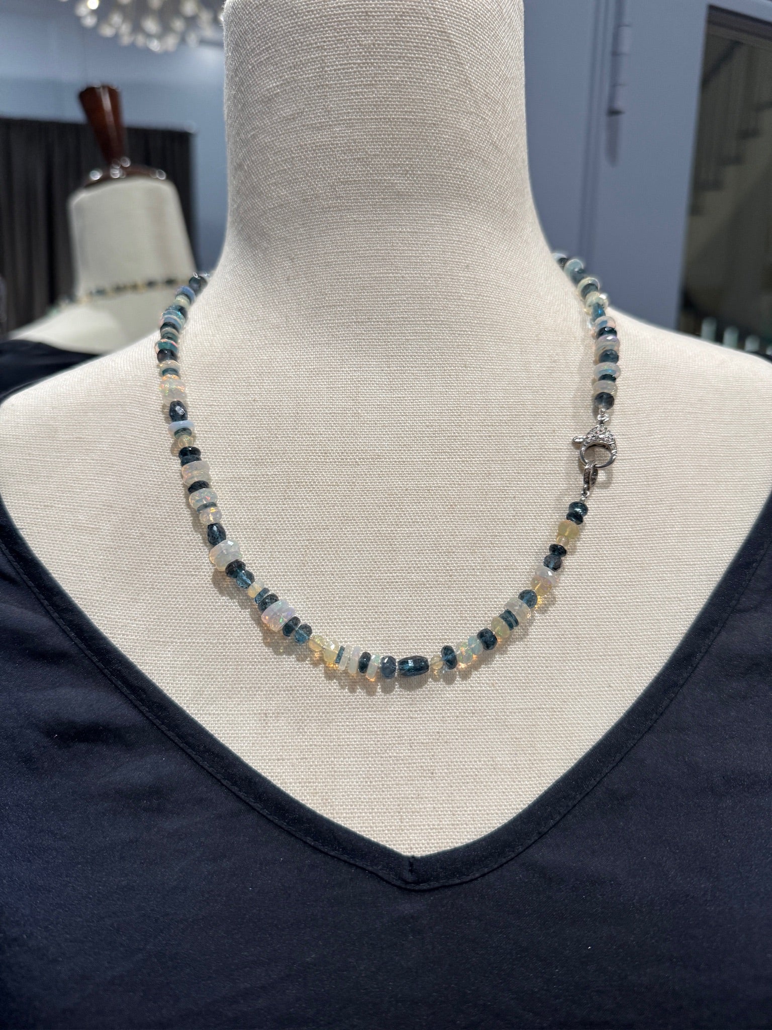 Close-up view of Ethiopian opal and London blue topaz necklace on cream mannequin, highlighting the contrast between luminous white opal discs and rich blue topaz gemstones