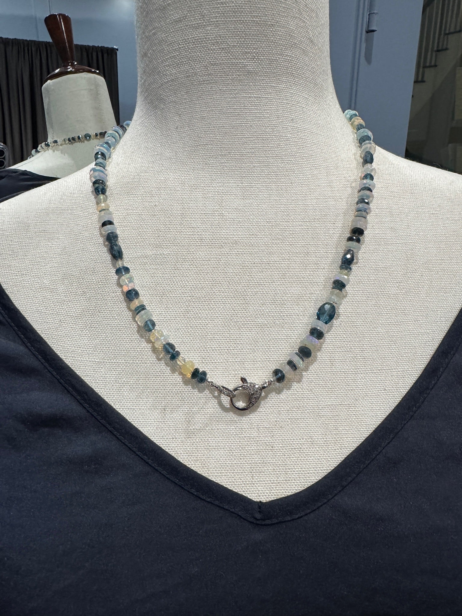 Detail shot of 21-inch opal and topaz necklace on mannequin, showcasing the intricate sterling silver toggle clasp and alternating pattern of iridescent Ethiopian opals and blue topaz