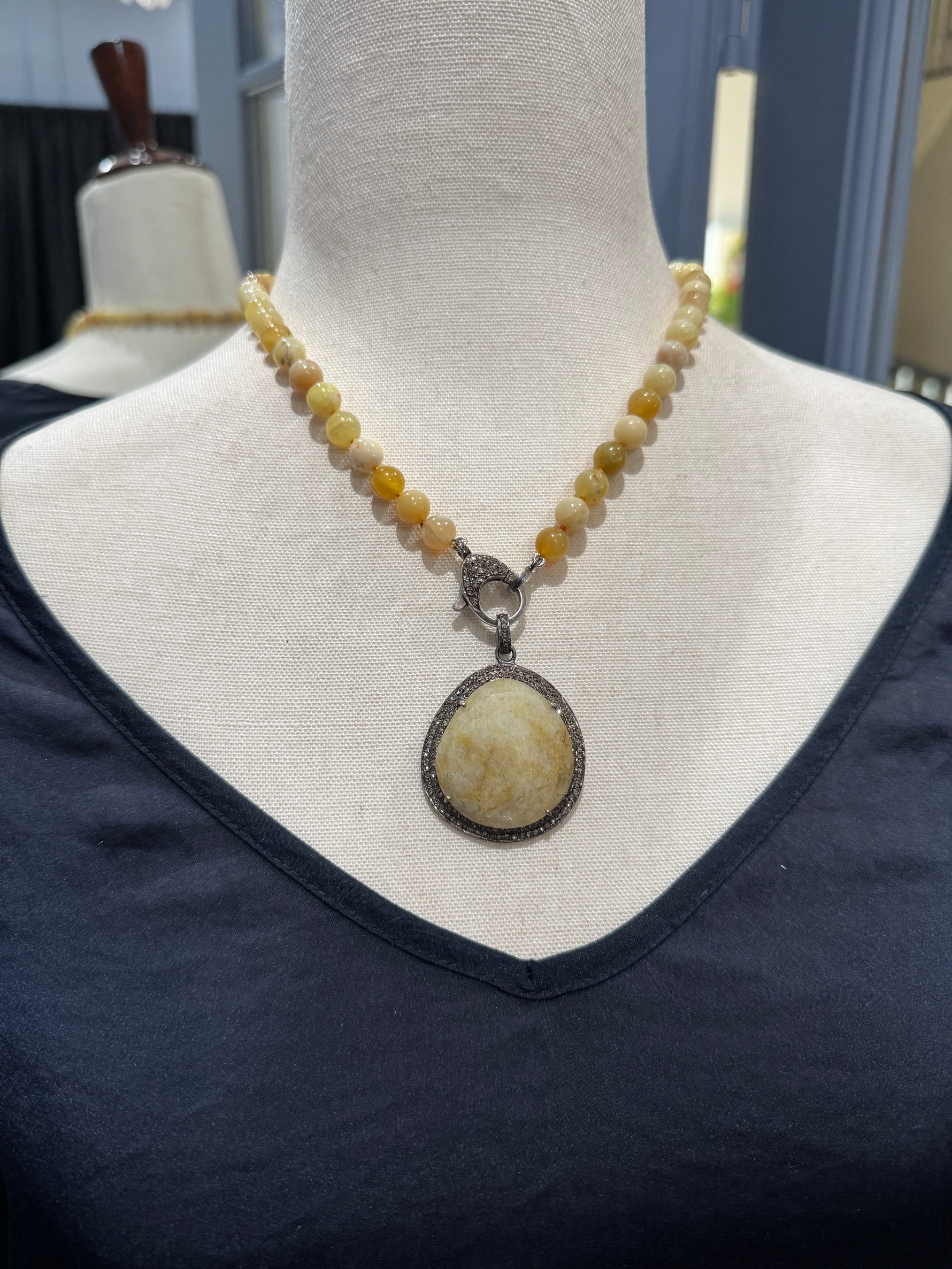 Yellow opal and aquamarine necklace displayed on cream fabric mannequin showing 18-inch length with diamond-encircled pendant centerpiece