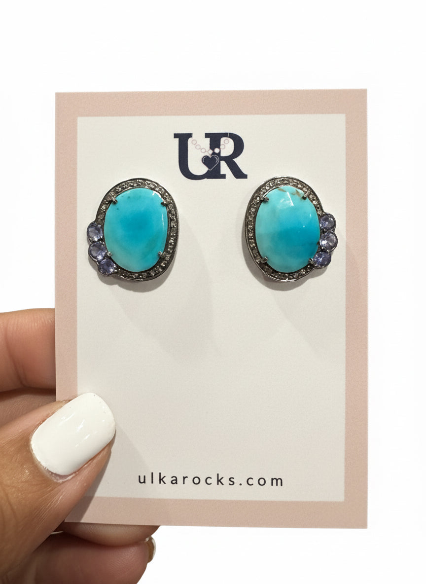 Turquoise earrings on a branded card held by a hand.
