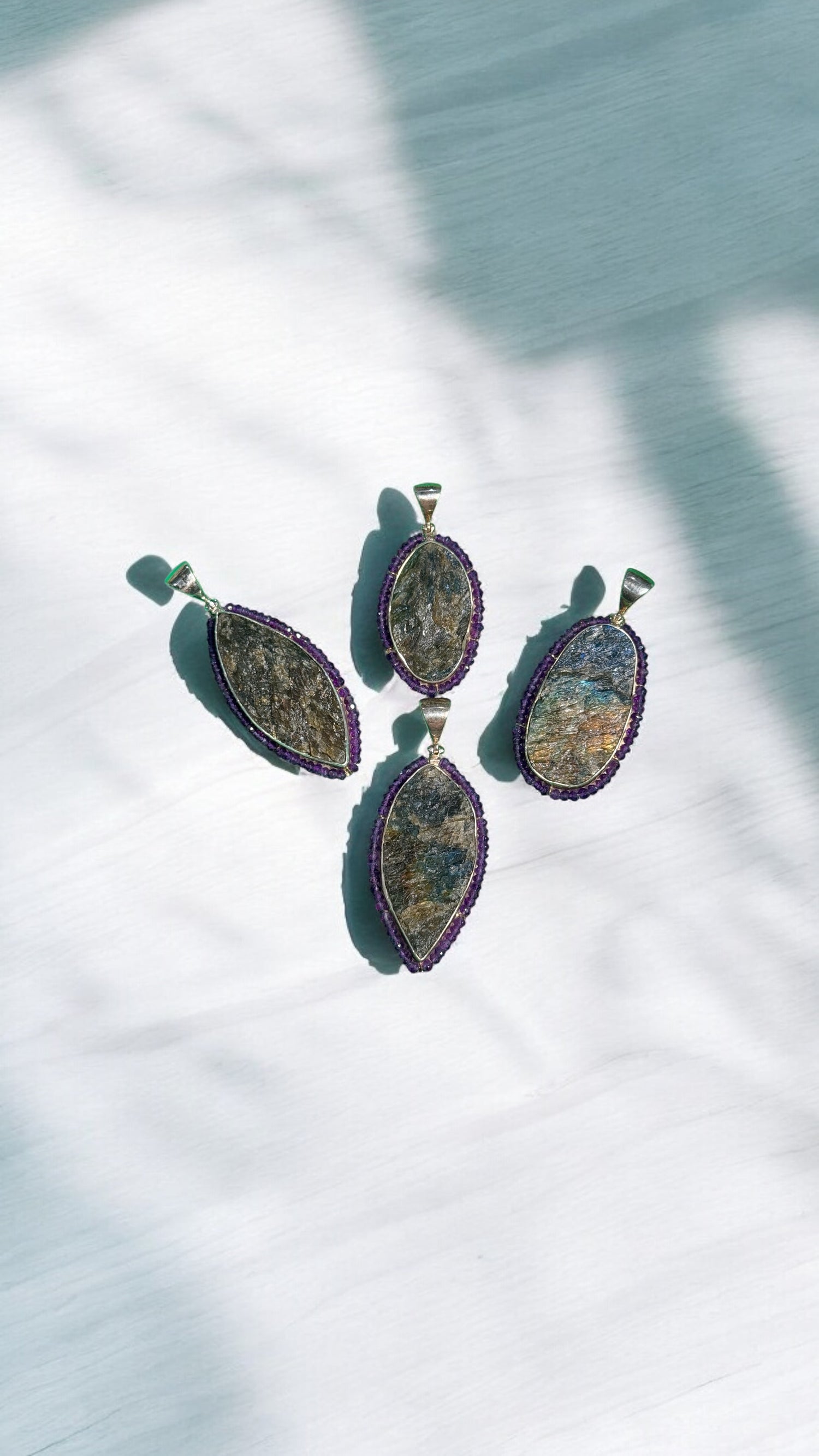 Four raw labradorite pendants with purple amethyst borders in sterling silver settings displayed on white marble surface with dramatic shadows