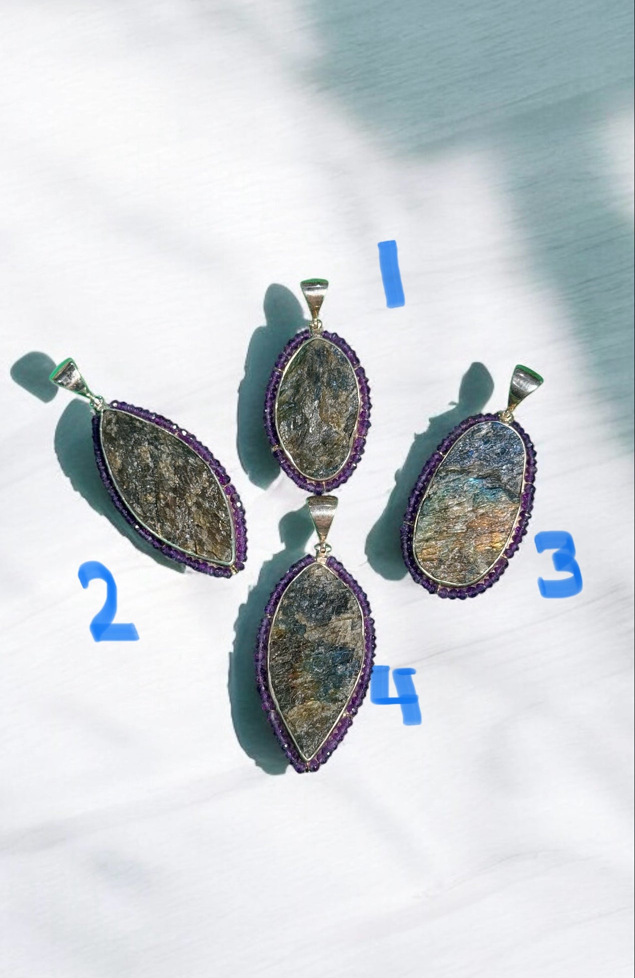 Four numbered raw labradorite pendants with purple amethyst stone borders in sterling silver, arranged on white marble with cloud shadows