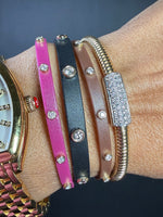 Close-up of a wrist wearing multiple colorful bracelets with diamond-like stones on a dark background.