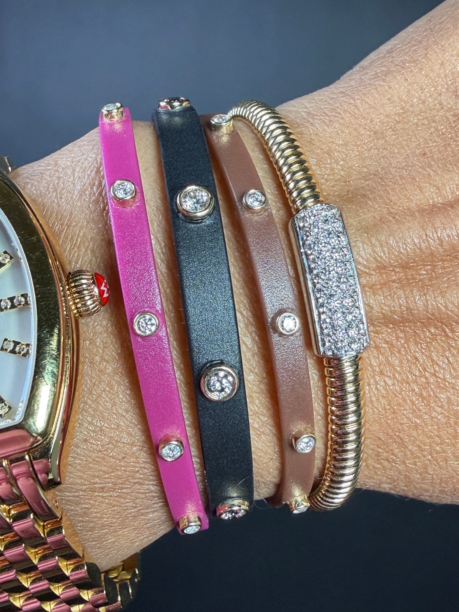 Close-up of a wrist wearing multiple colorful bracelets with diamond-like stones on a dark background.