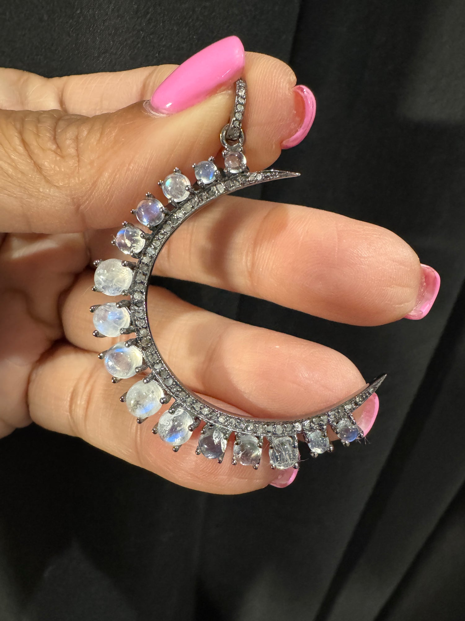 Hand holding crescent moon pendant featuring rainbow moonstone cabochons and diamonds in sterling silver setting with detailed chain clasp visible