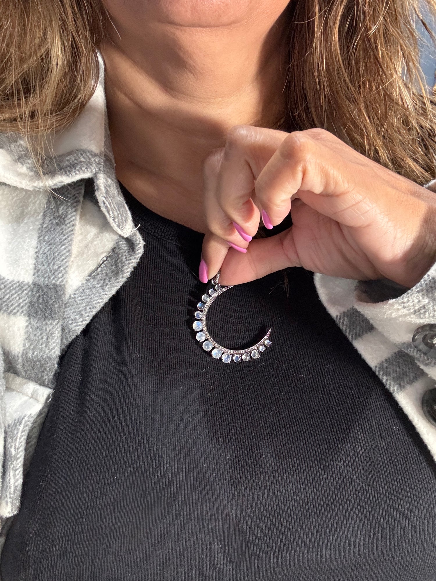Woman wearing moonstone diamond crescent moon pendant on sterling silver chain against black top, showing elegant neckline styling
